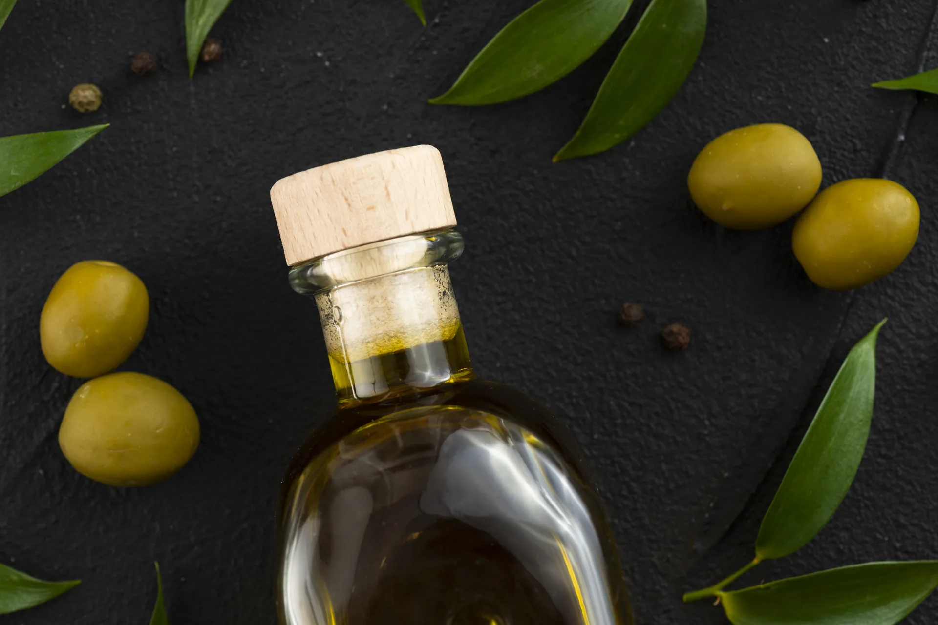 Elegante Kristallflasche mit goldgelbem Premium-Olivenöl auf dunklem Marmor, daneben ein Olivenzweig