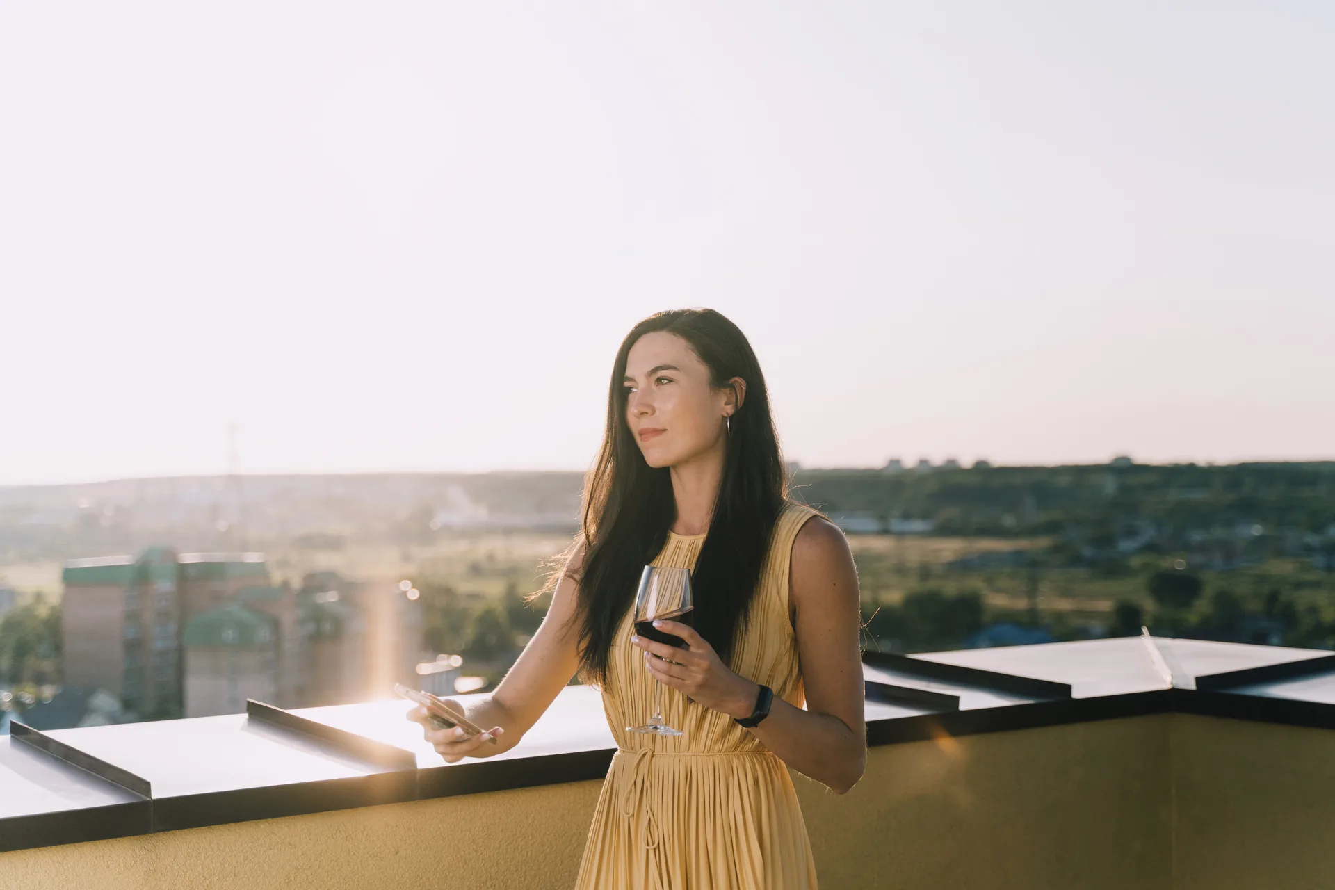 Elegant gekleidete Person genießt allein den Blick über die abendliche Skyline einer Großstadt von einer Dachterrasse