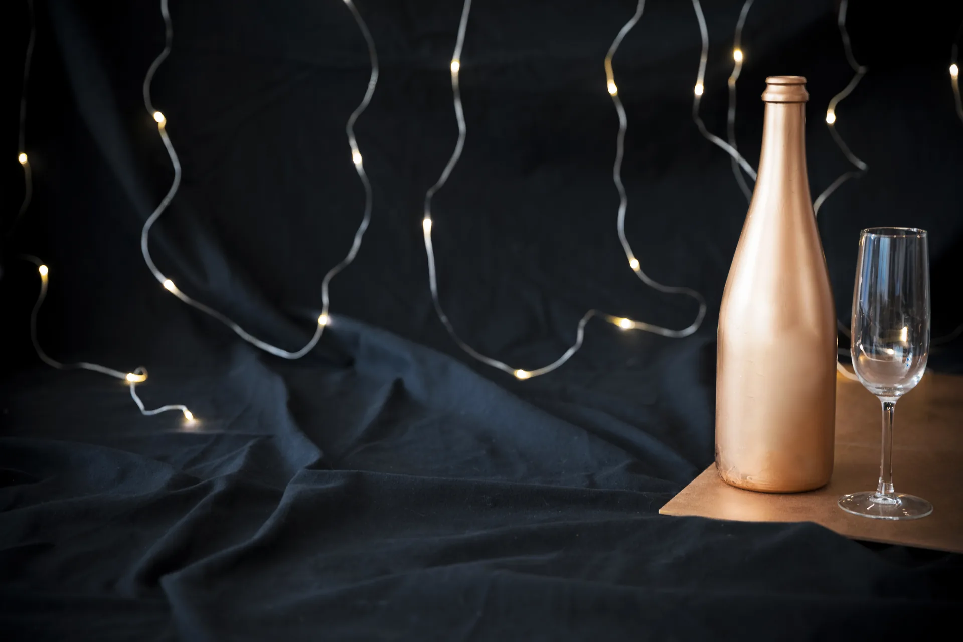 Edle Champagnerflasche mit gefüllten Kristallgläsern auf dunklem Marmor im warmen Kerzenlicht