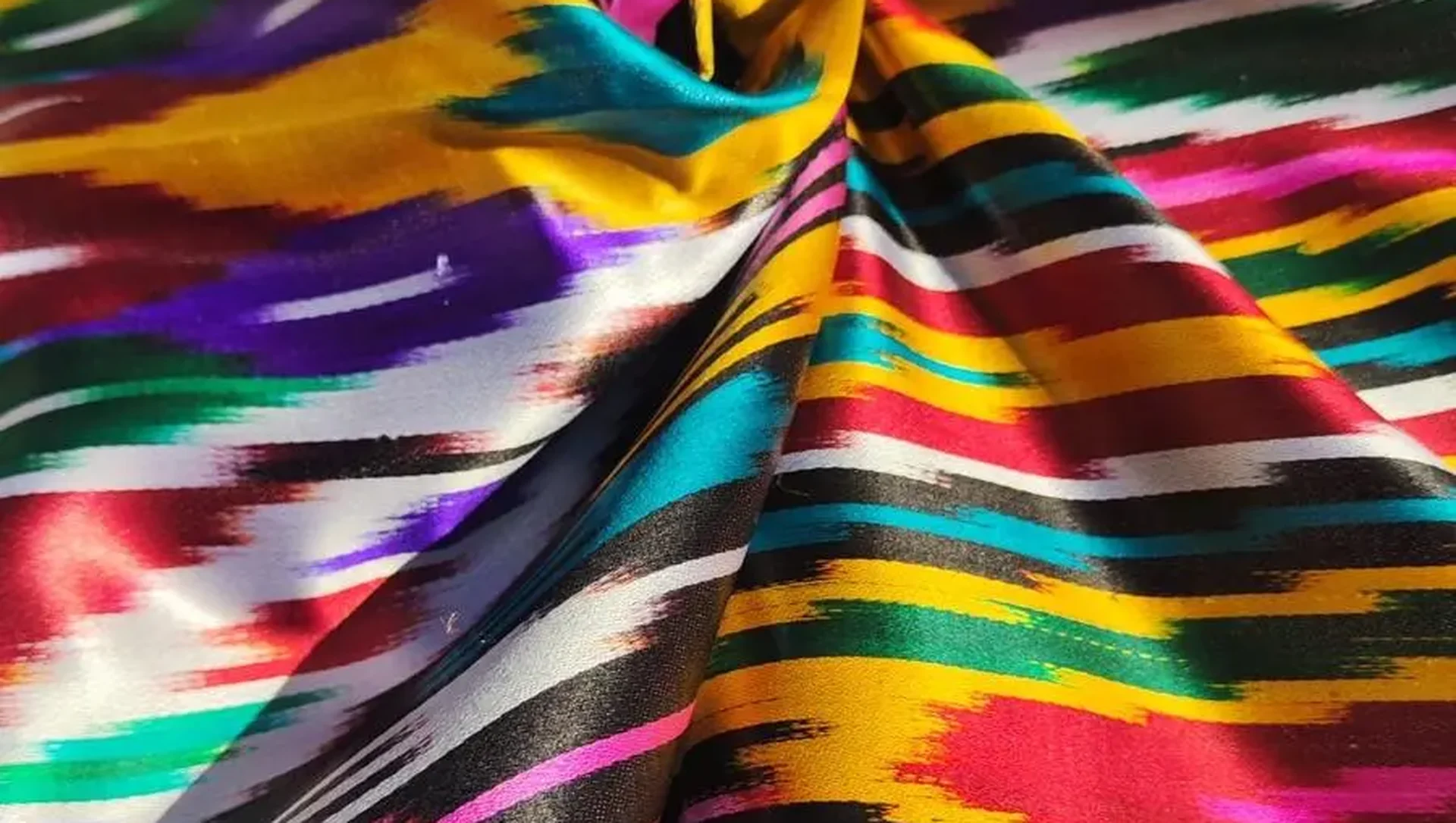 Glänzende Ikat-Seide in Gold, Violett und Türkis, kunstvoll in Falten gelegt