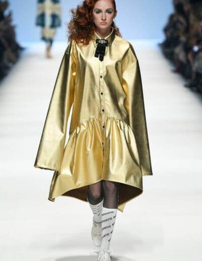 Eine Frau läuft in einem goldenen Mantel über den Laufsteg.