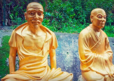 Drei Statuen buddhistischer Mönche sitzen auf einem Felsen.