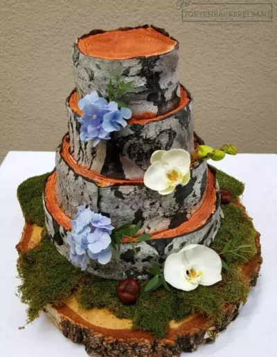 Ein dreistöckiger Kuchen mit Blumen und Moos oben drauf.