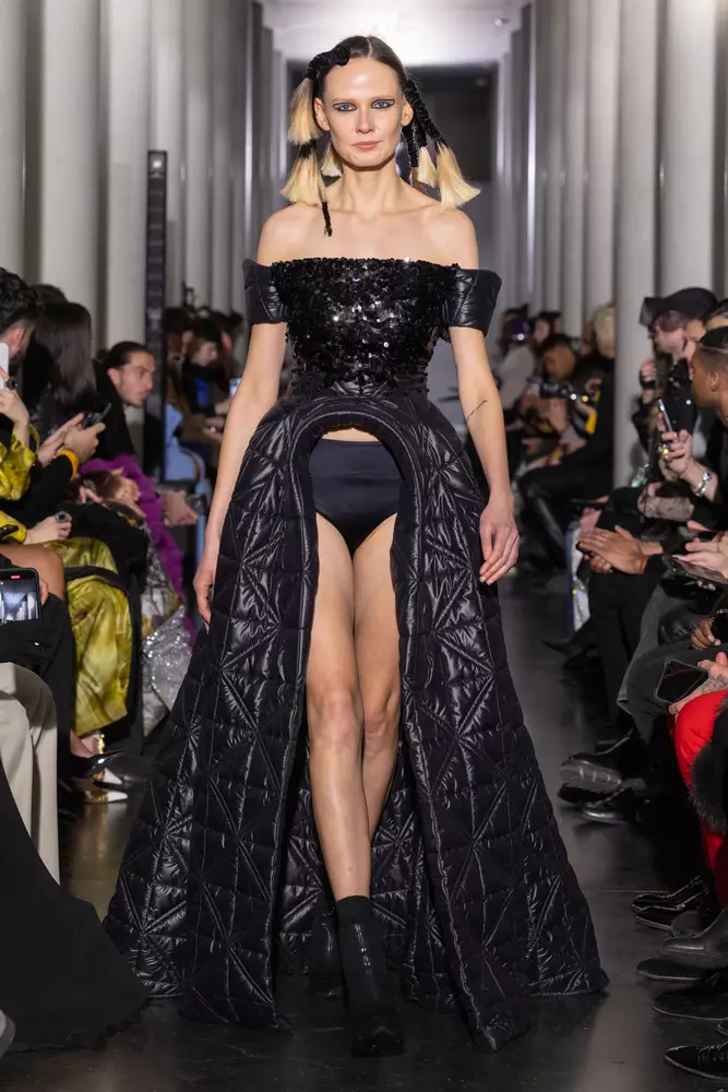 Ein Model läuft in einem schwarzen Kleid über den Laufsteg.
