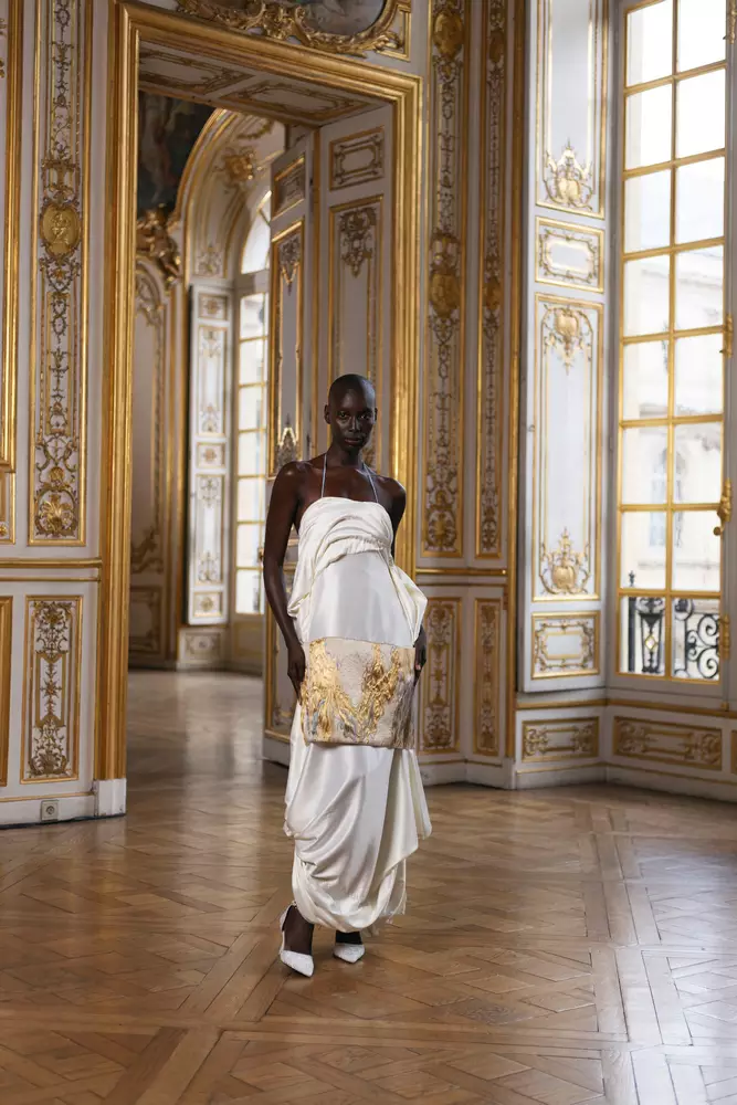 Eine Frau in einem weißen Kleid steht in einem reich verzierten Raum.
